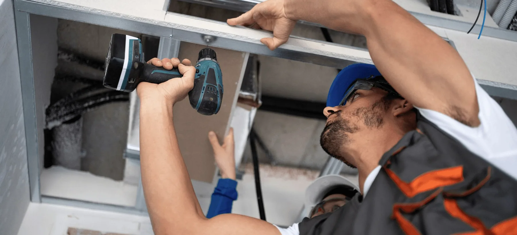 A technician drilling into a ceiling duct.