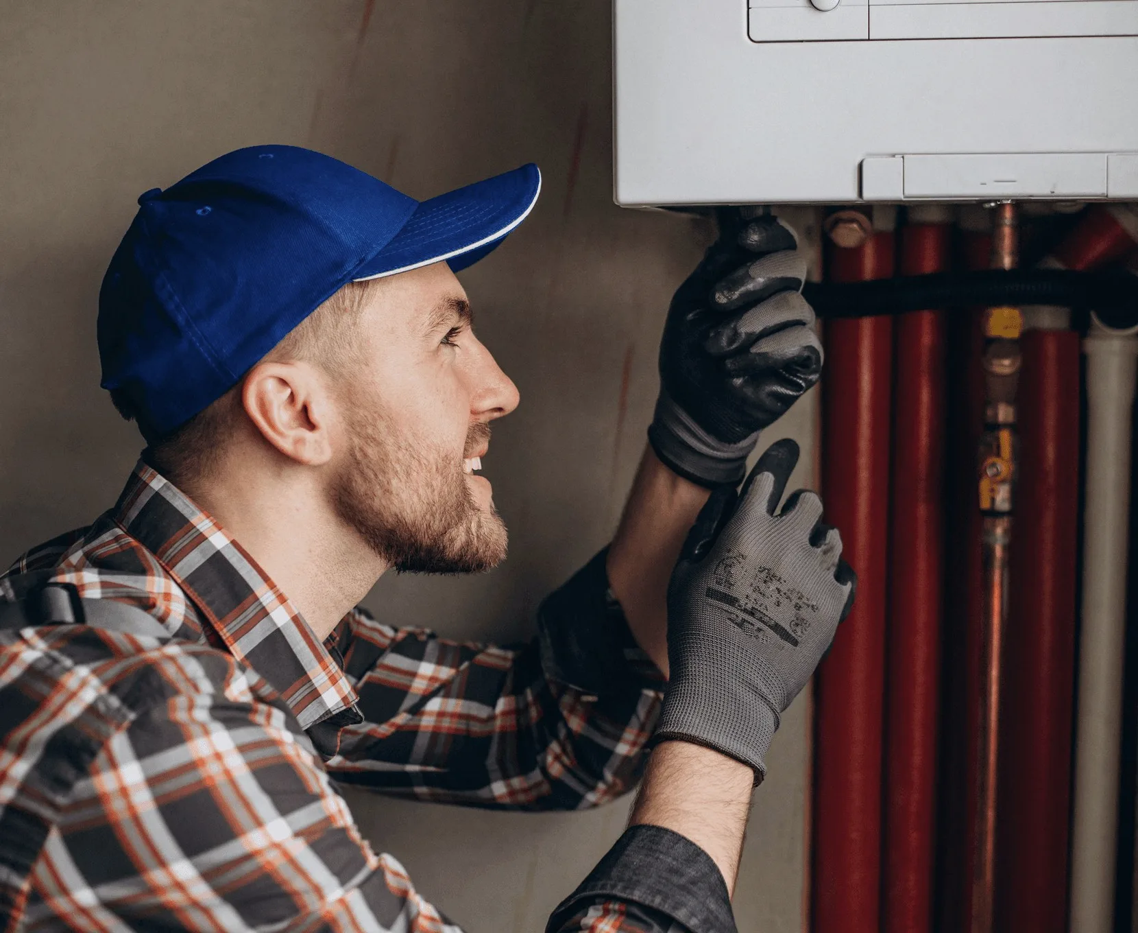 A technician in a blue cap working at red pipes.