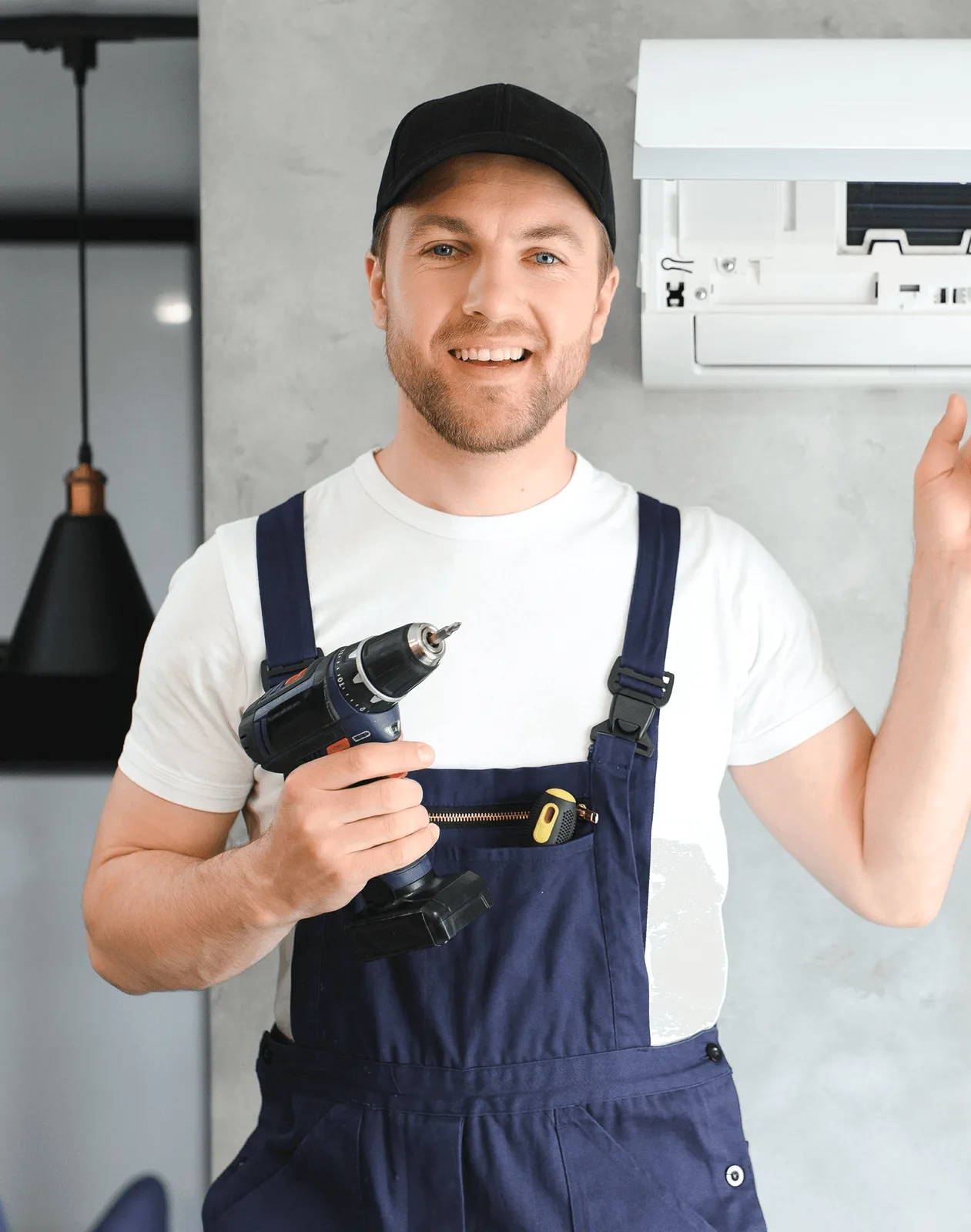 A smiling technician holding a drill beside a wall unit.