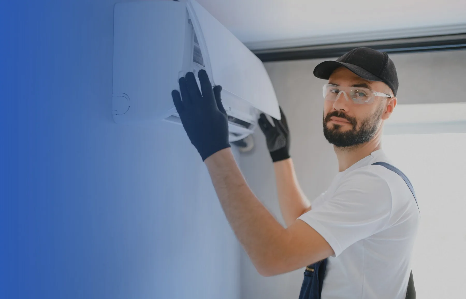 A technician in a cap and safety glasses fitting a wall unit.