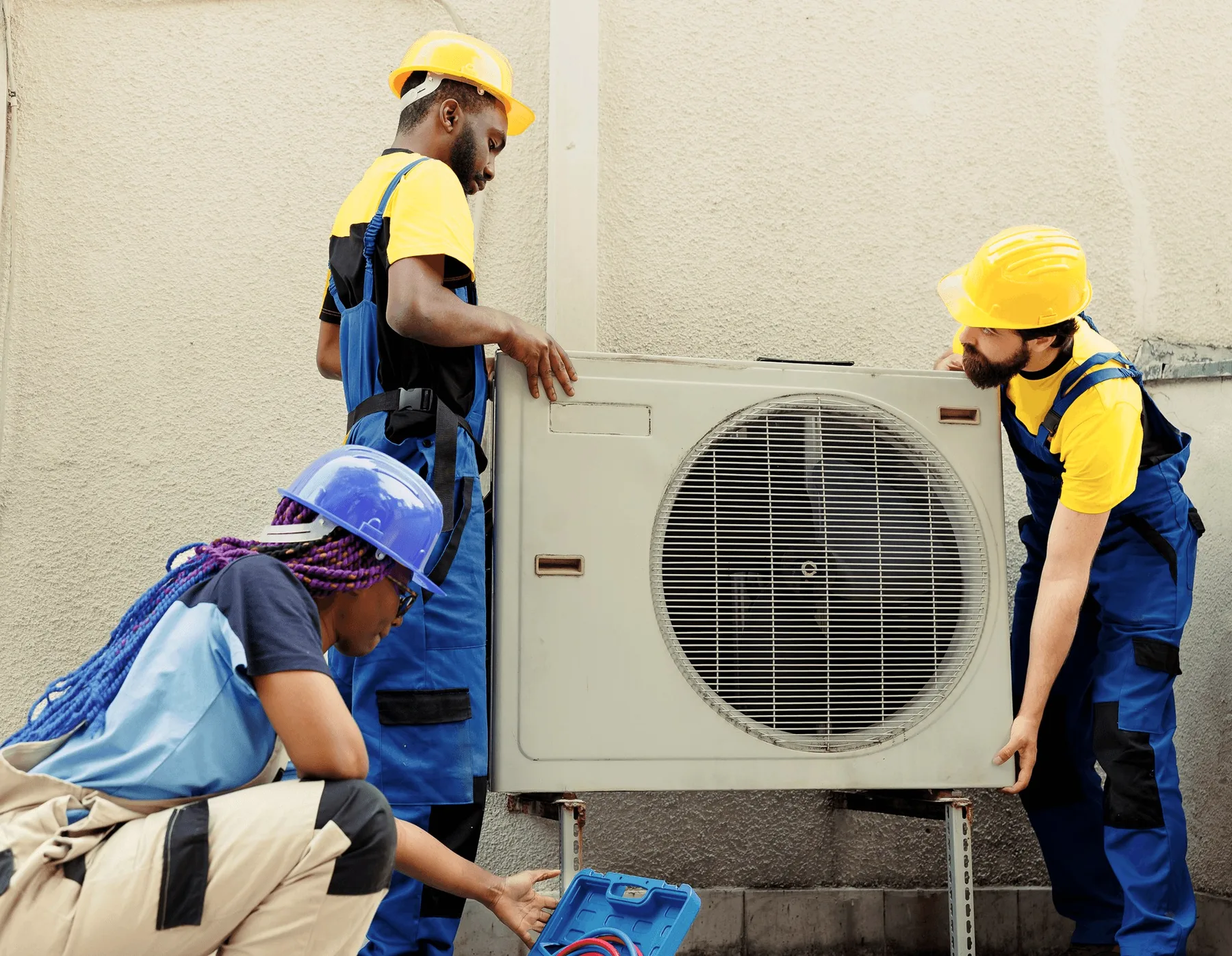 Two technicians carrying an outdoor unit past a wall.
