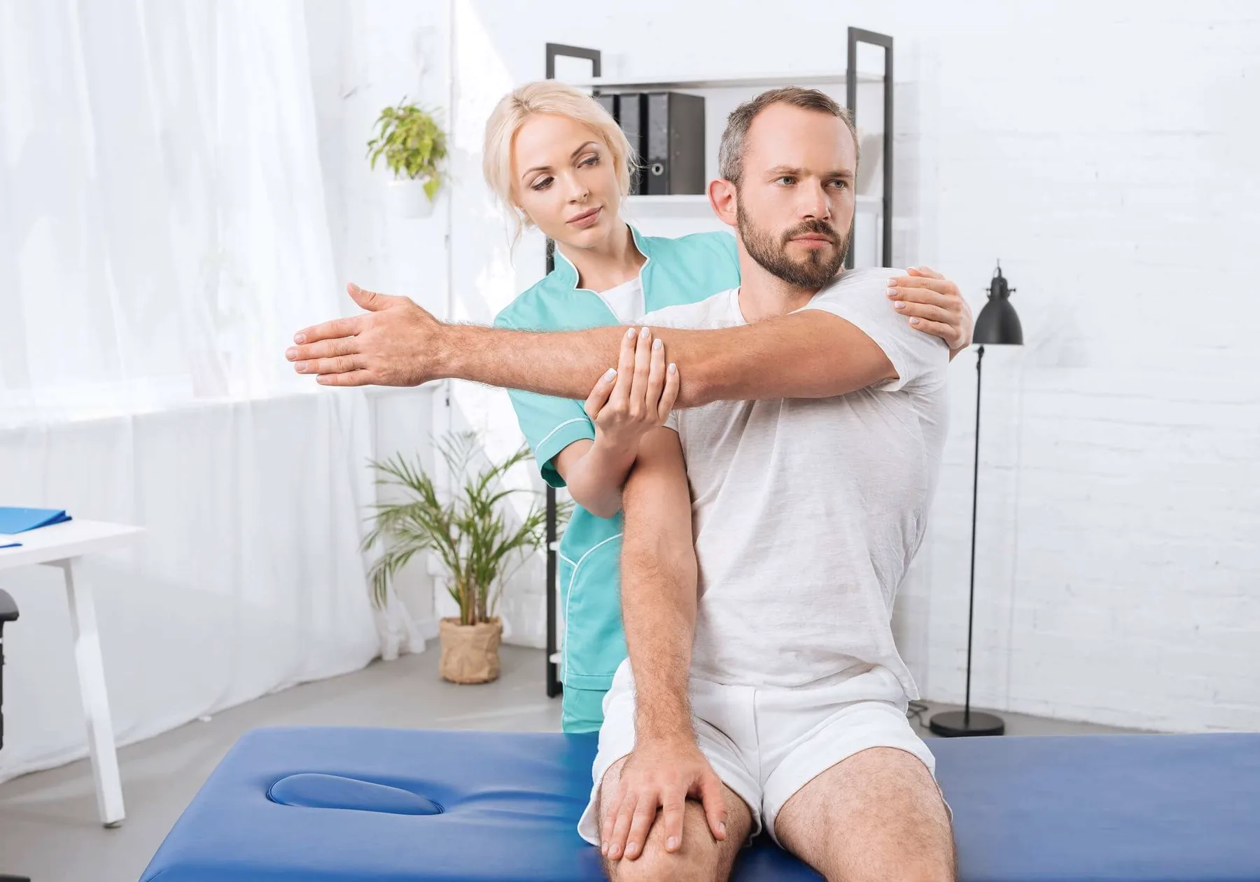 A physiotherapist guiding a man's arm behind his head.