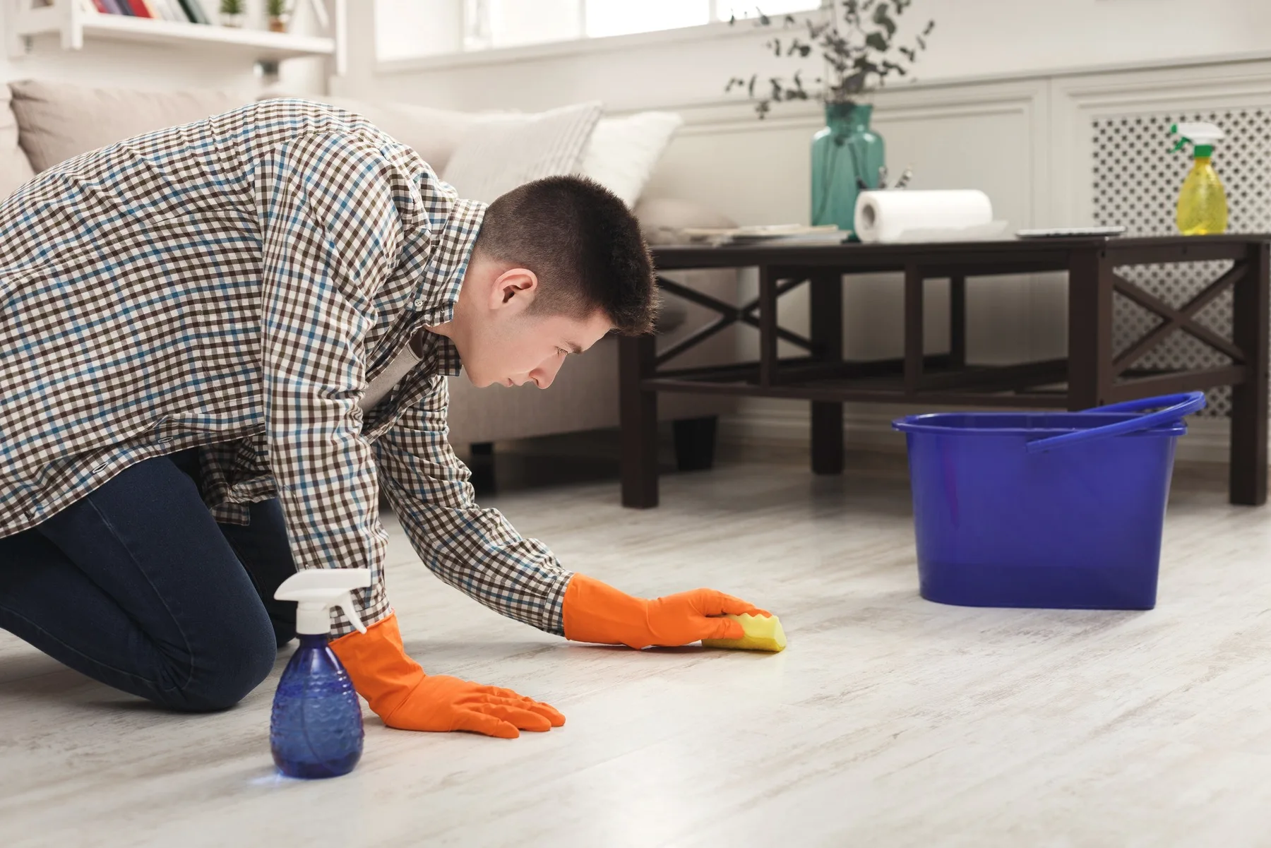 A cleaner on their knees wiping a wooden floor, a blue bucket beside.