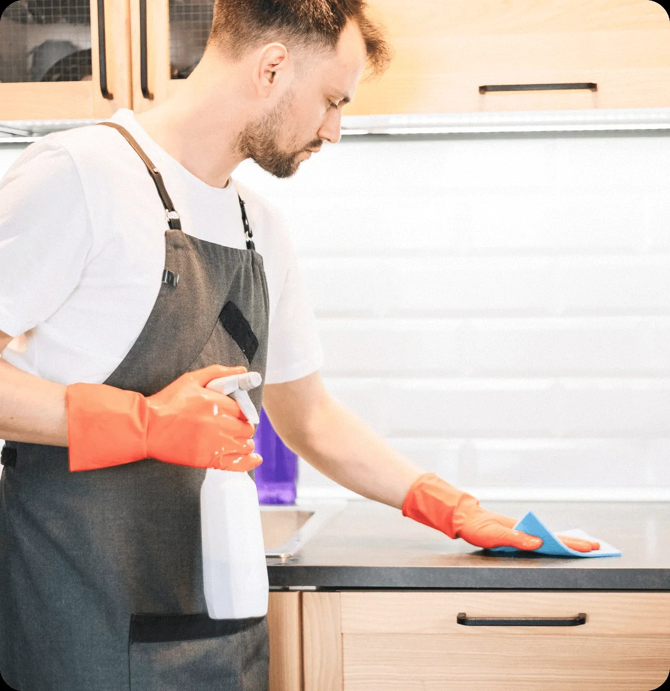 A cleaner in an apron wiping a kitchen counter.