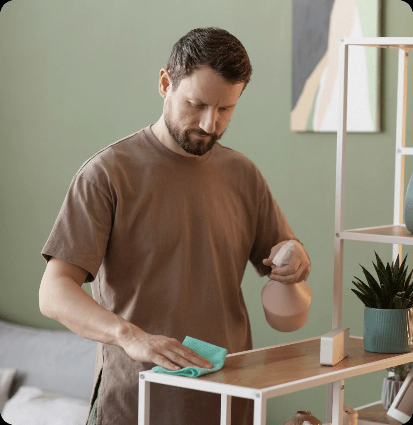 A man dusting a shelf beside a plant.