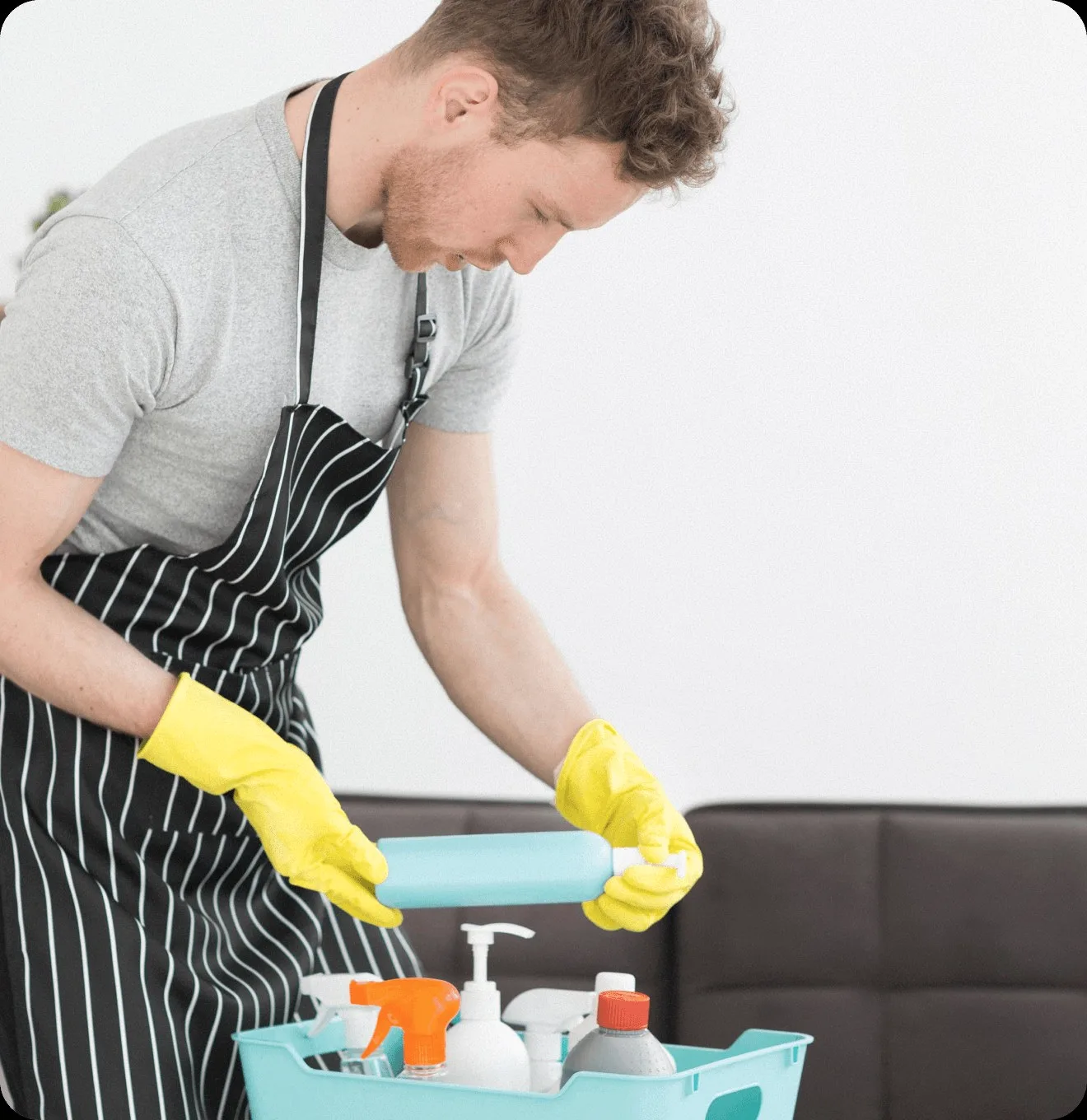 A cleaner in a striped apron with a caddy of bottles.