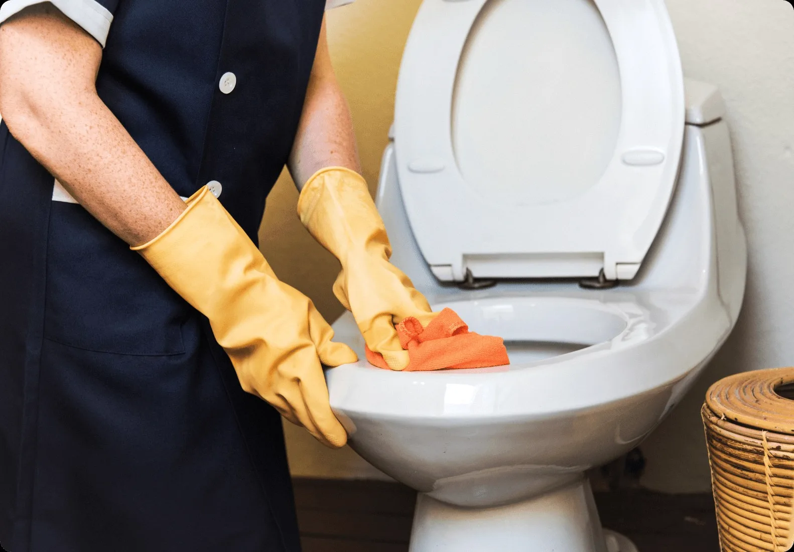 Yellow gloves wiping a white toilet.