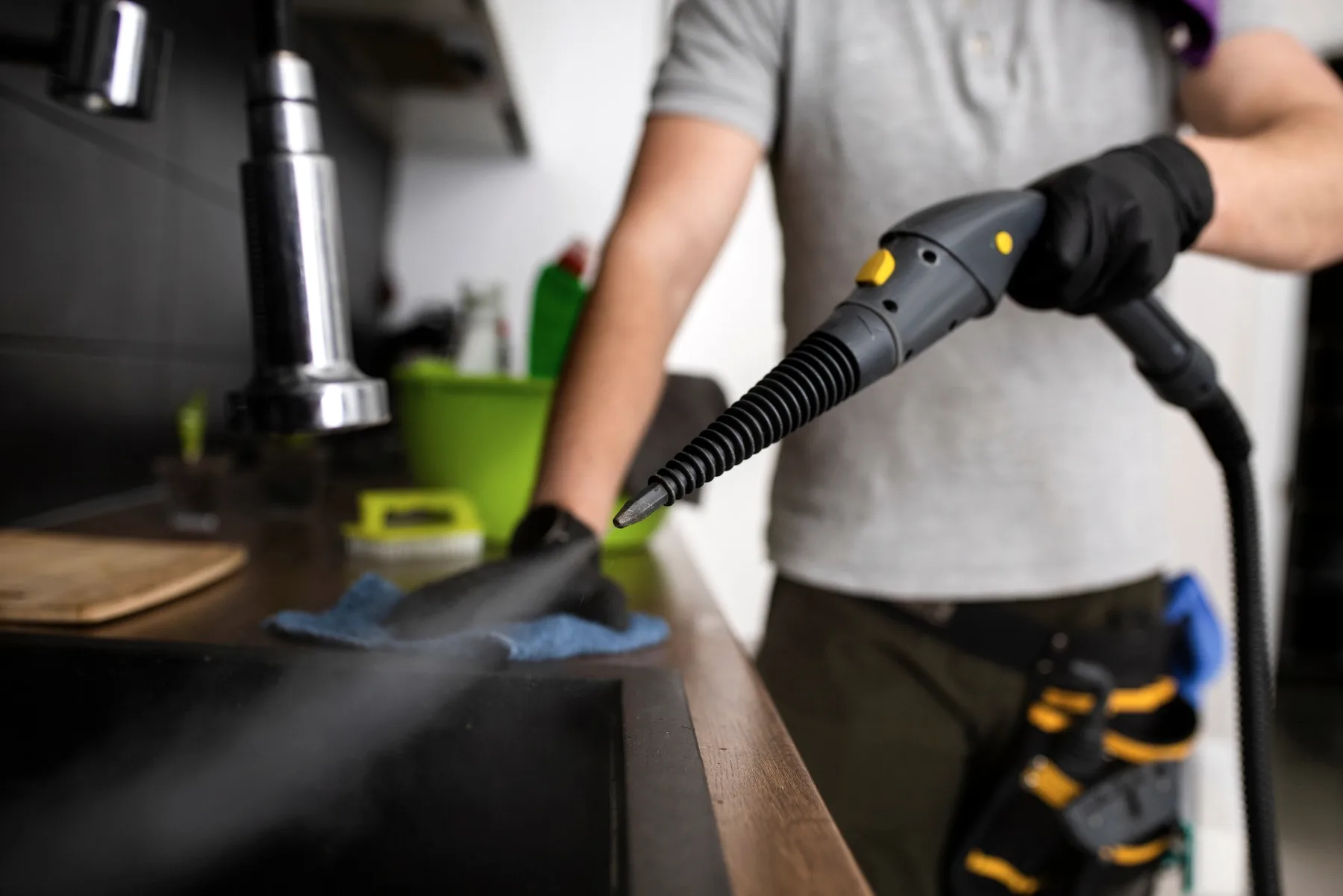 Gloved hands with a steam cleaner at a counter.
