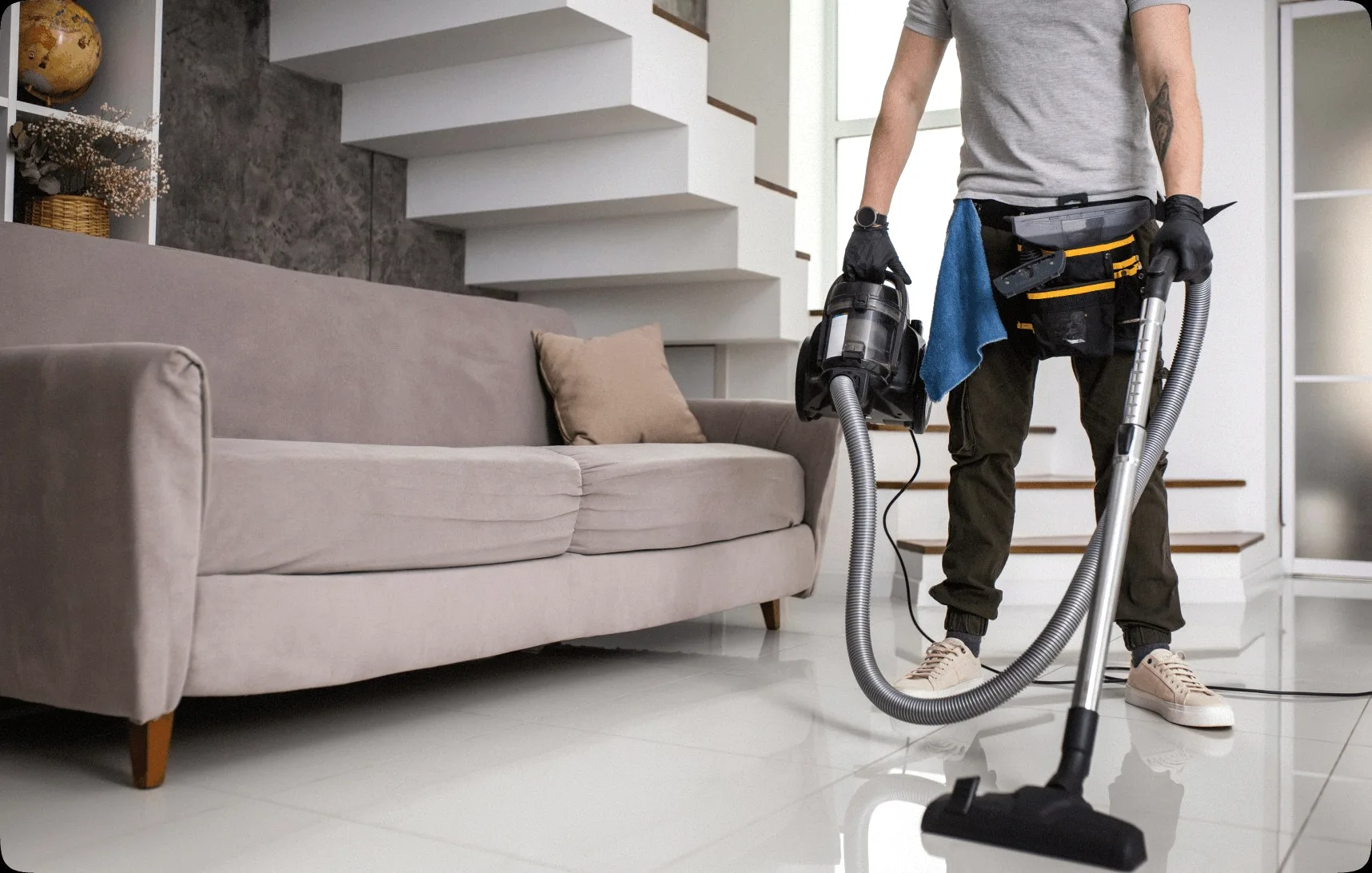 A cleaner vacuuming beside a beige sofa.