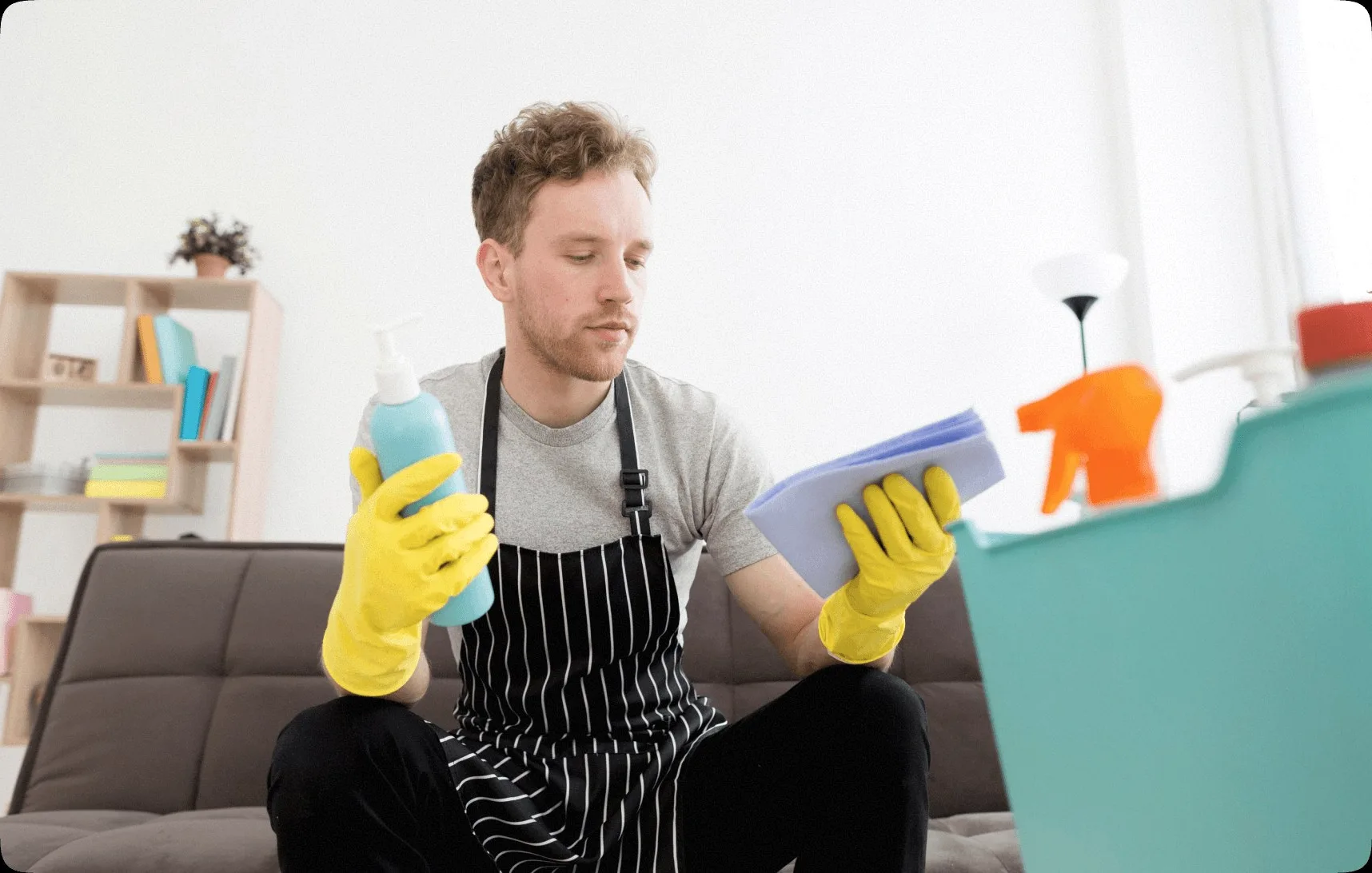 A cleaner in a striped apron sitting with a bottle and a sponge.