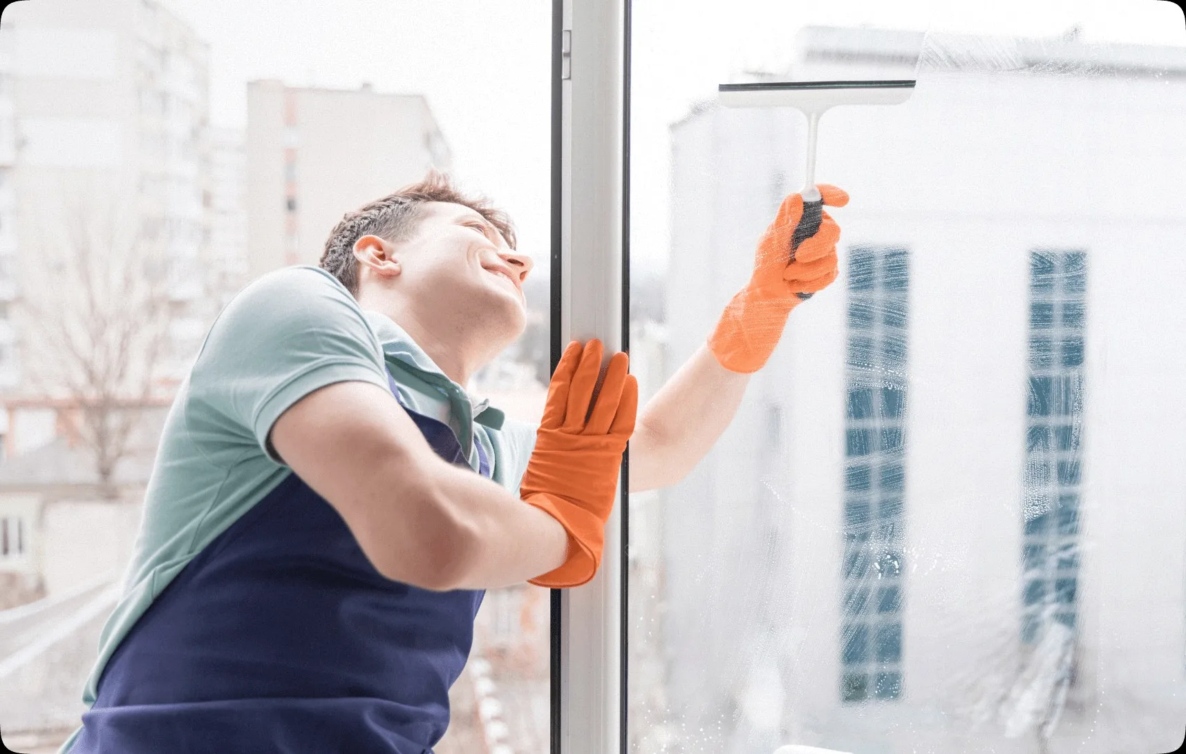 A cleaner in orange gloves squeegeeing a window.