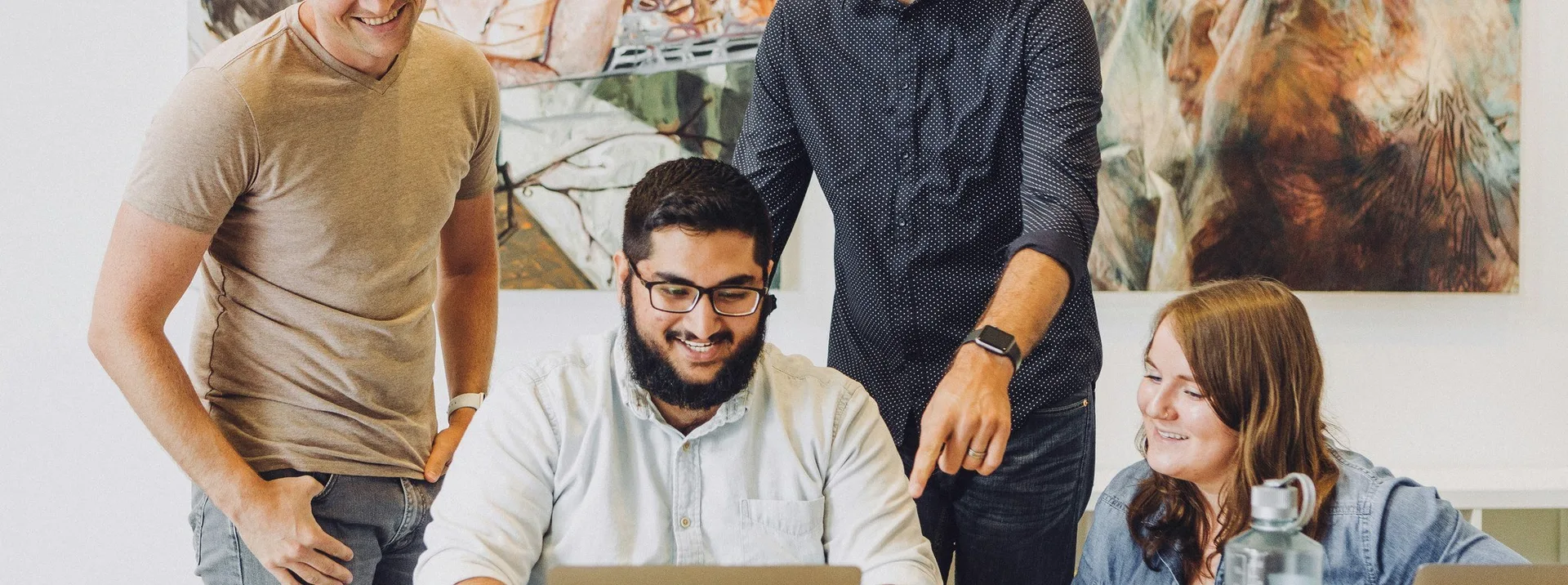 Four colleagues laughing around a laptop.