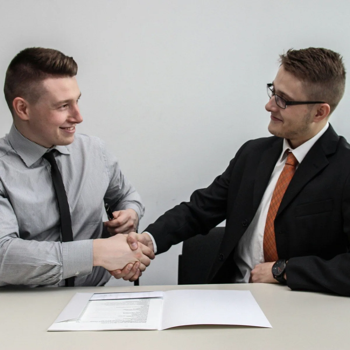 Two men in shirts and ties laughing at a desk.
