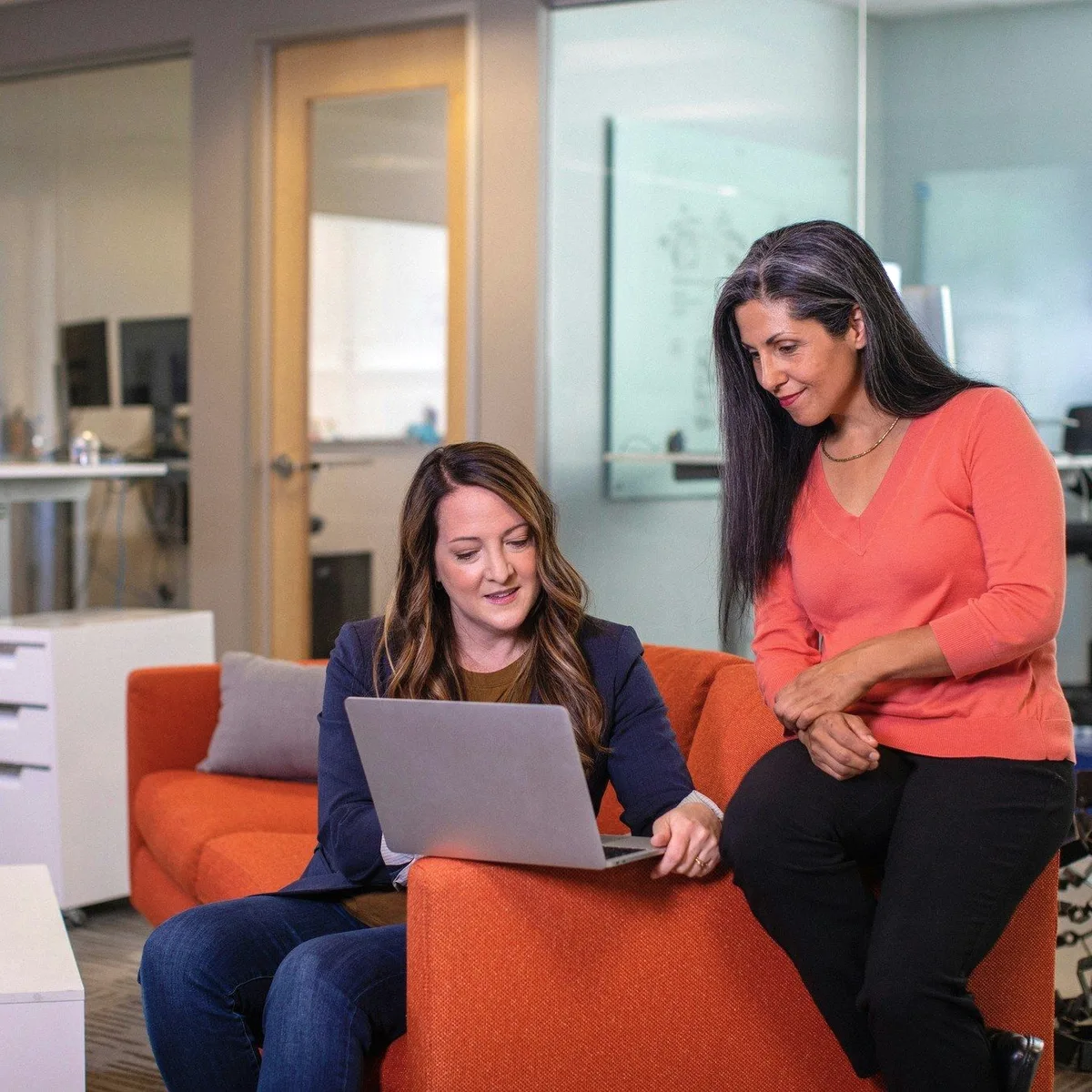Two colleagues on an orange sofa with a laptop.