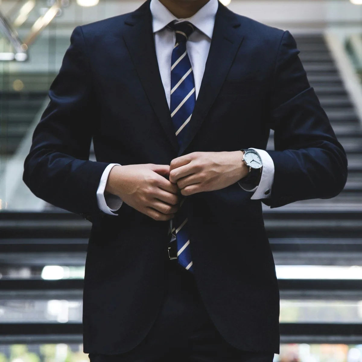 A man in a dark suit buttoning his jacket on a staircase.