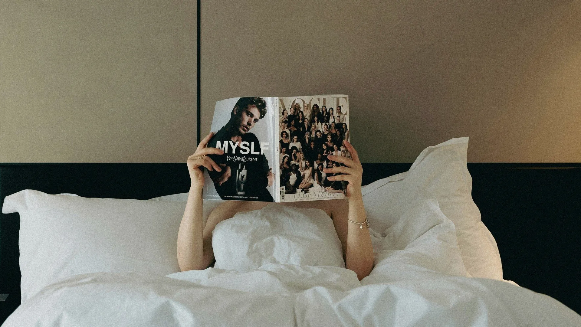 A person in bed holding a magazine over their face.