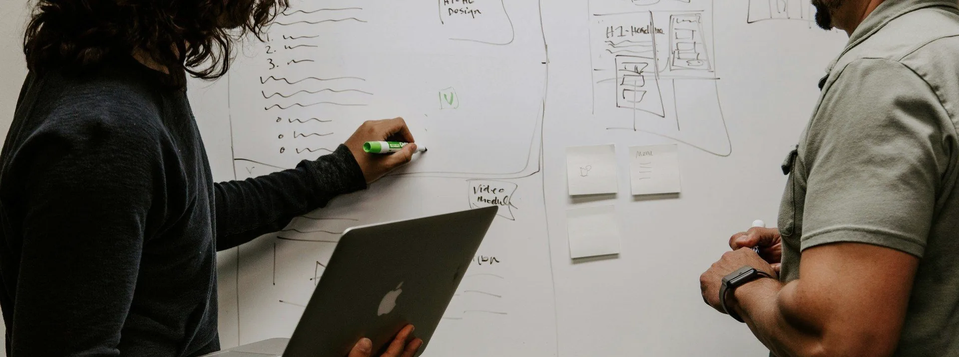 Two people at a whiteboard with a laptop.