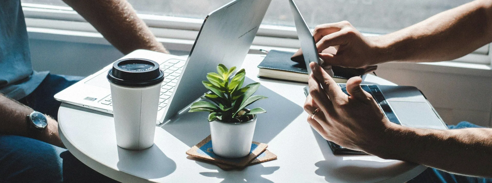 Hands over laptops and a coffee at a shared table.