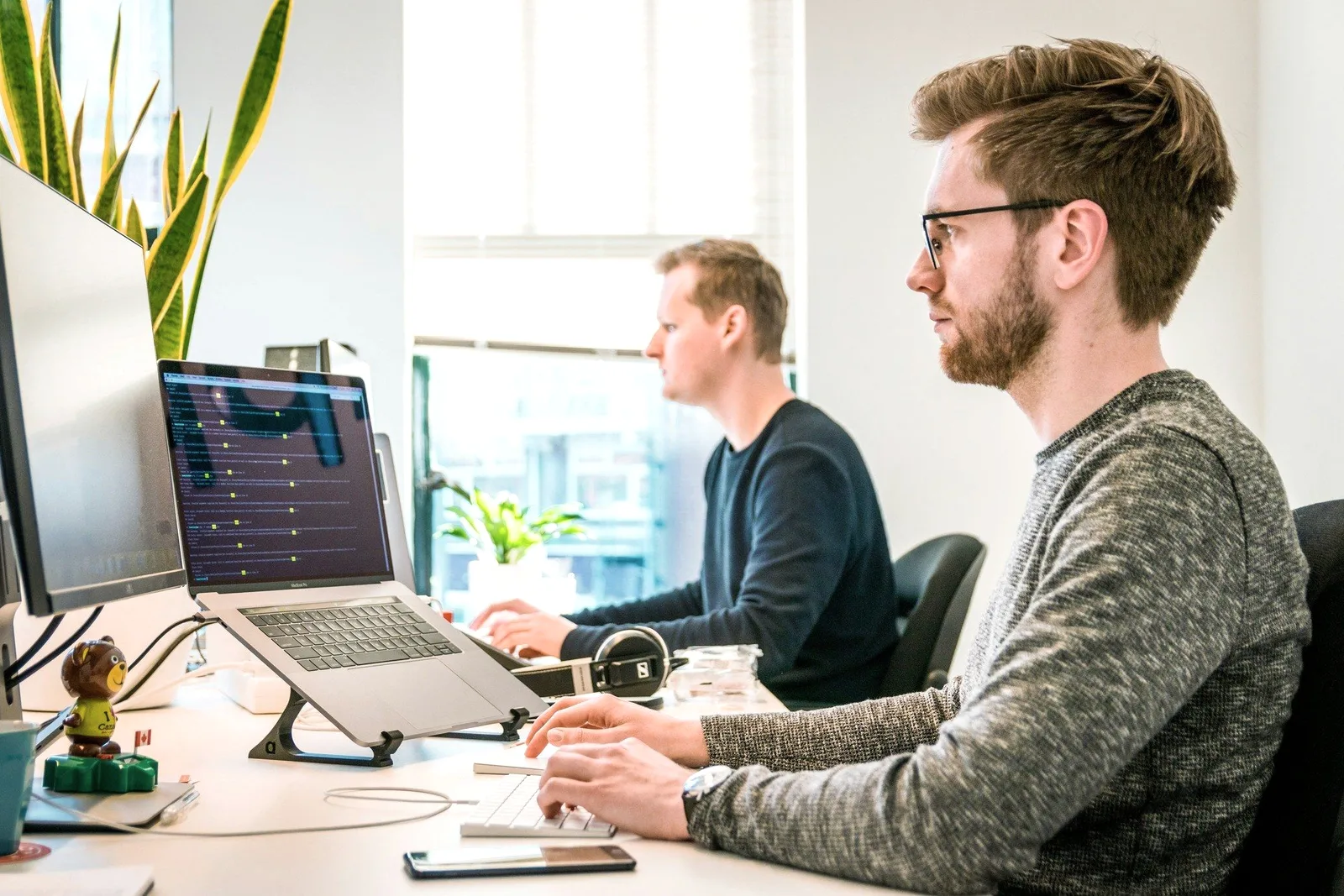 Two people working at laptops by a window.
