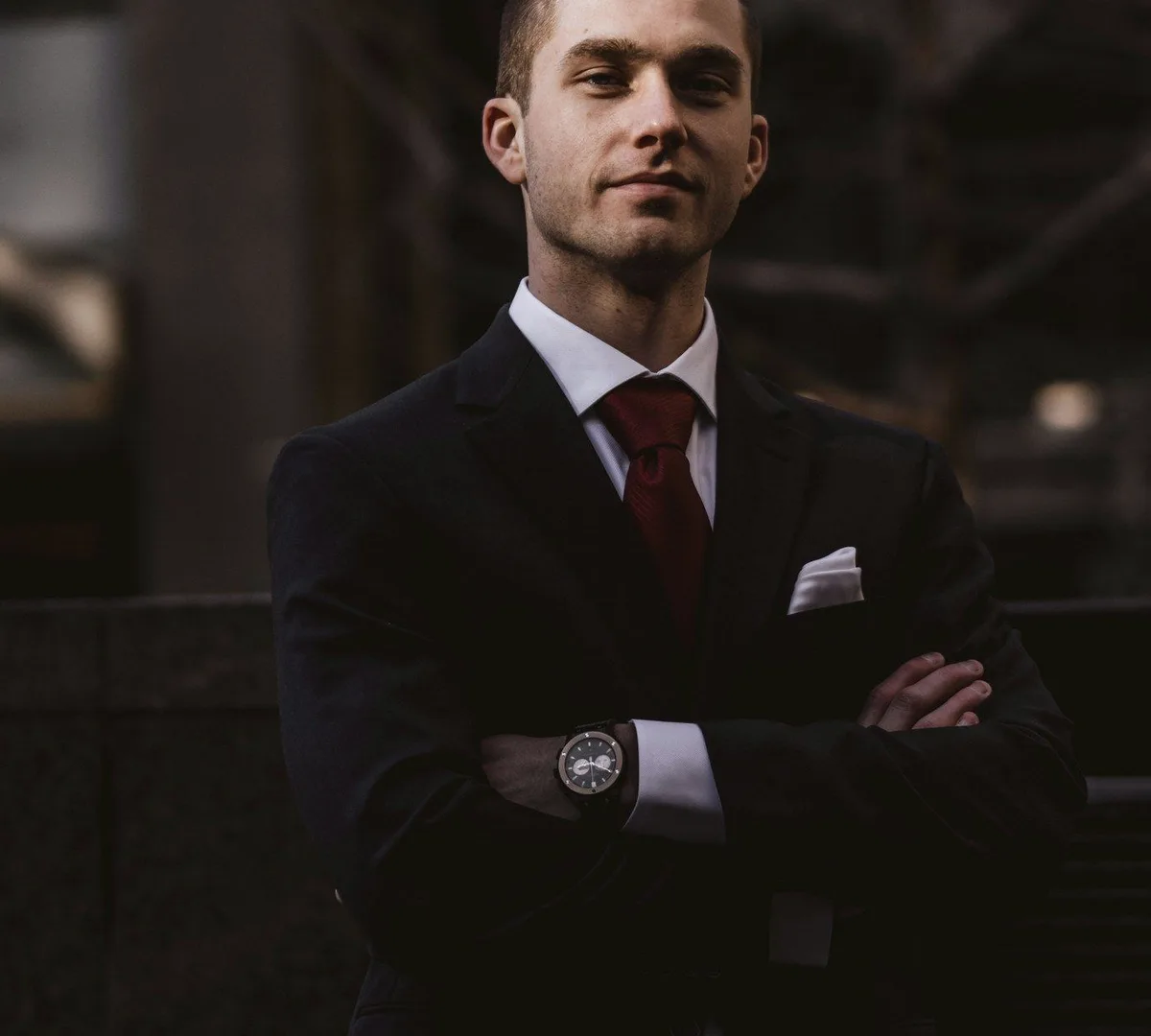 A man in a dark suit and red tie, arms crossed.