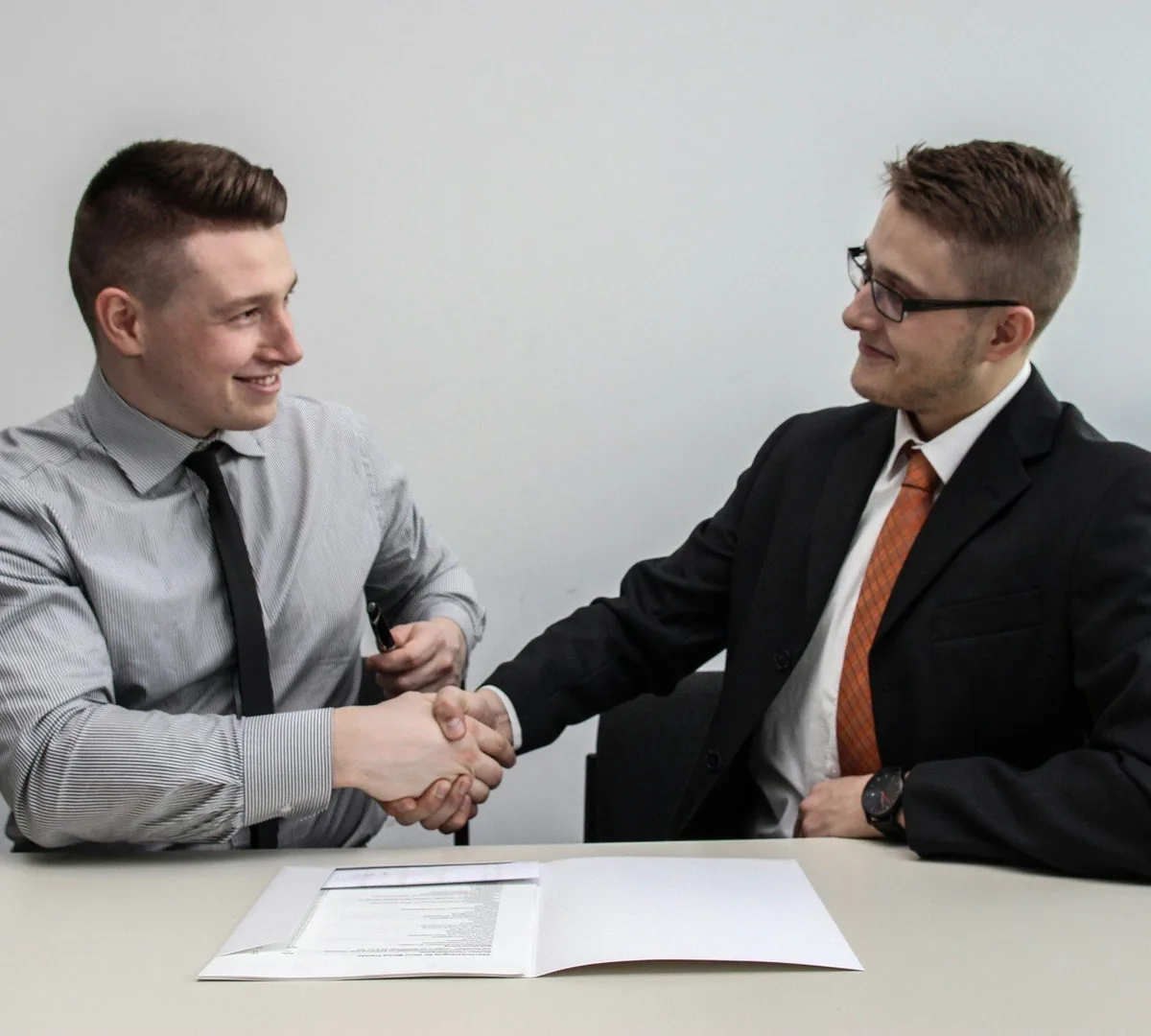 Two men shaking hands over a desk.