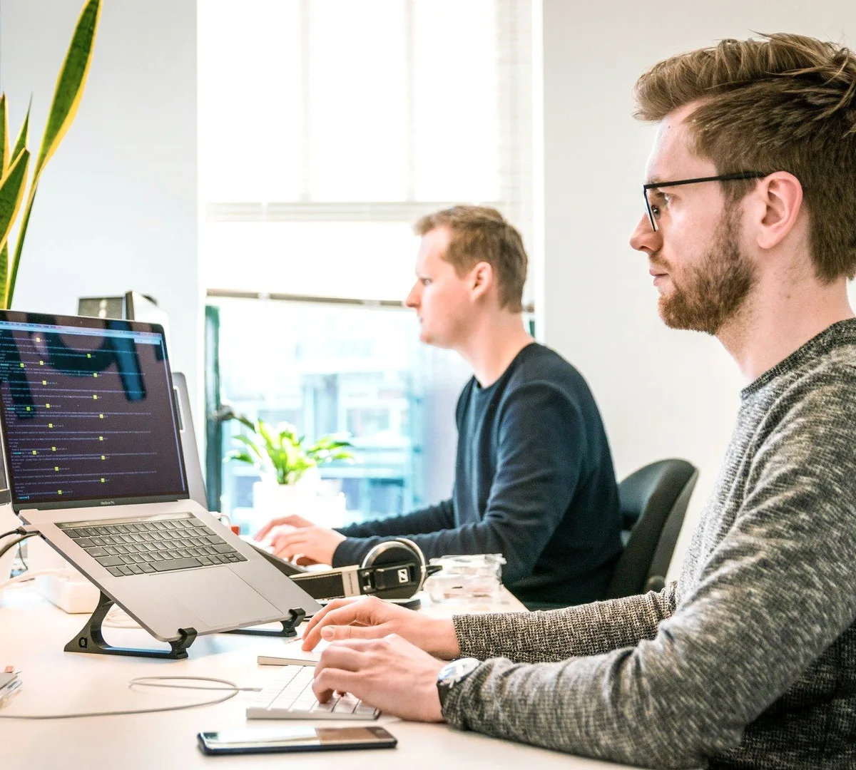 Two people at laptops by a window.