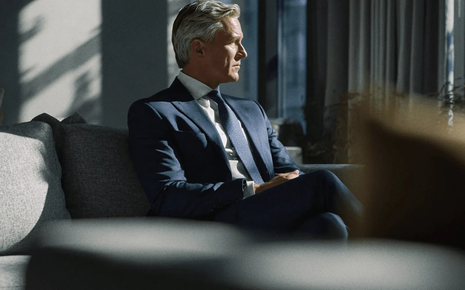 A man in a navy suit on a sofa.
