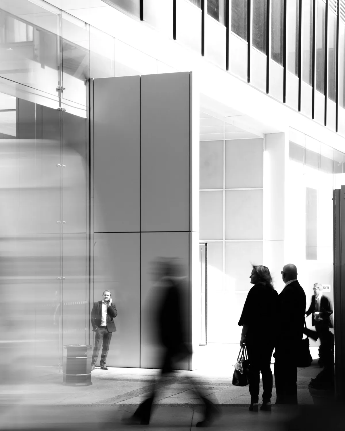 People walking through a glass lobby, in grey.
