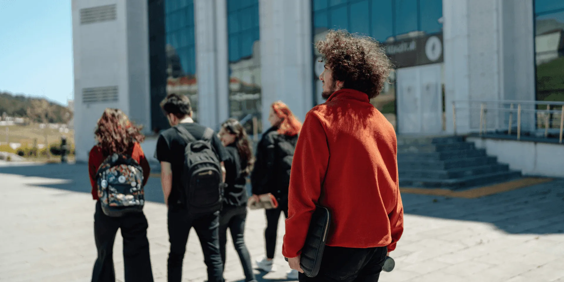 Students walking away across a campus square, one in a red hoodie.
