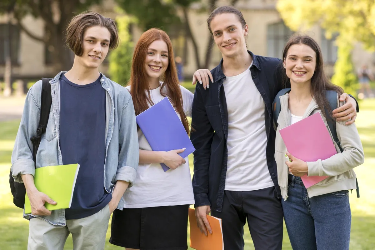 Five students with folders on a lawn.