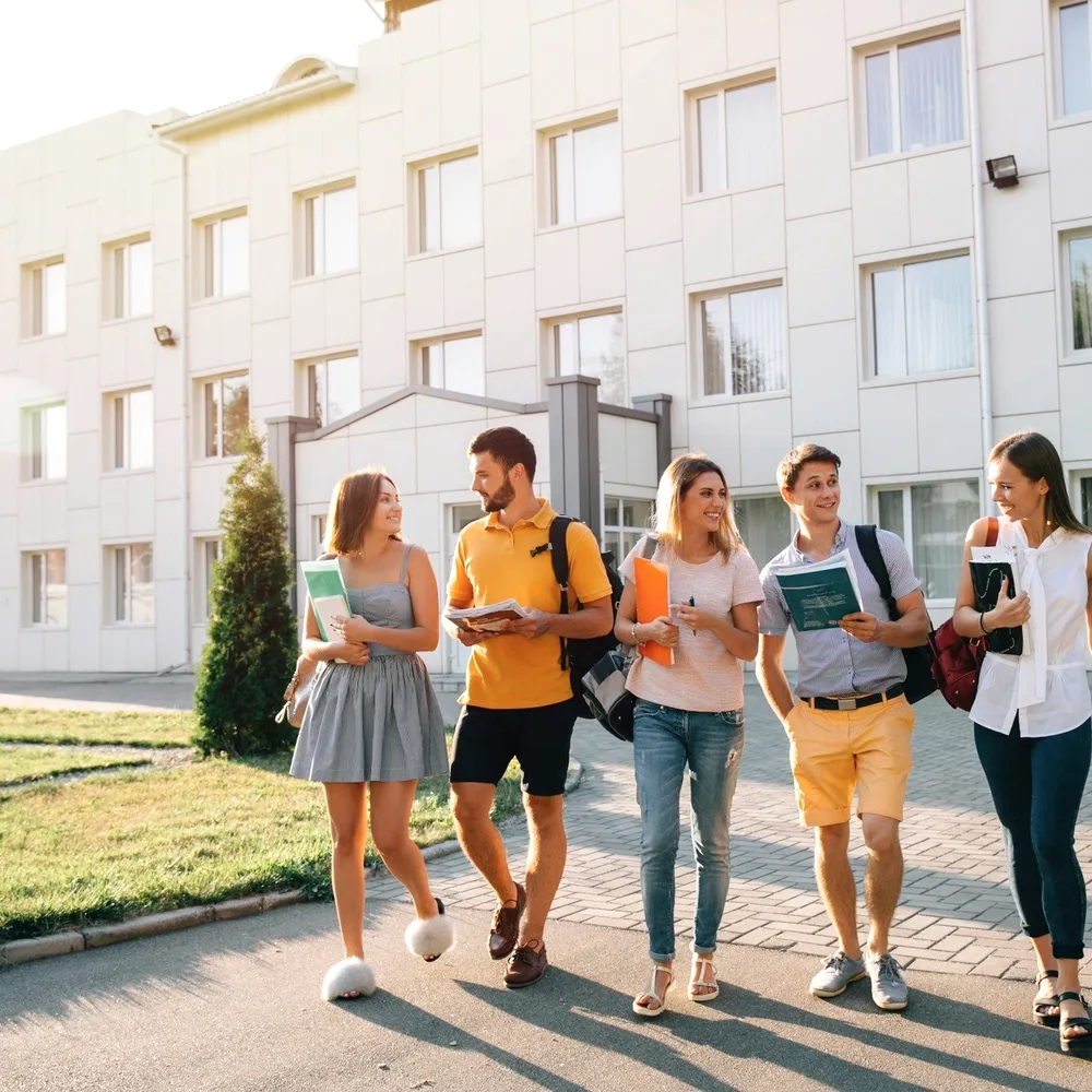 Five students walking past a white building.
