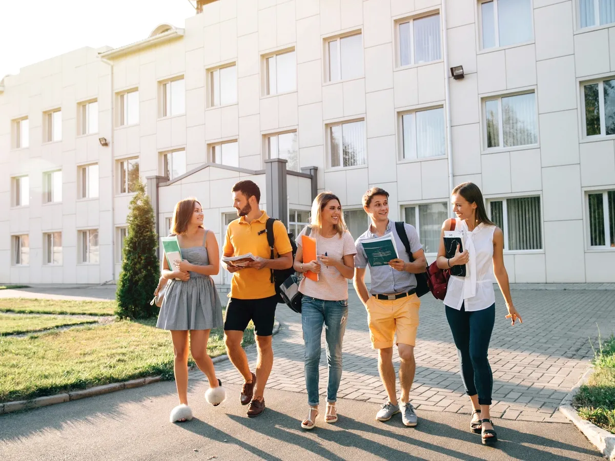 Five students walking past a white building.