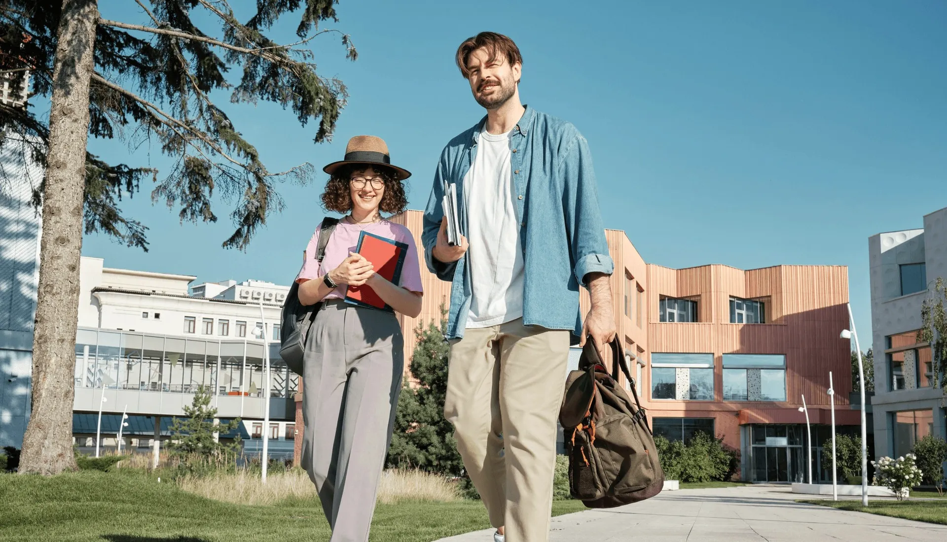 Two students with books and a bag on a campus path.