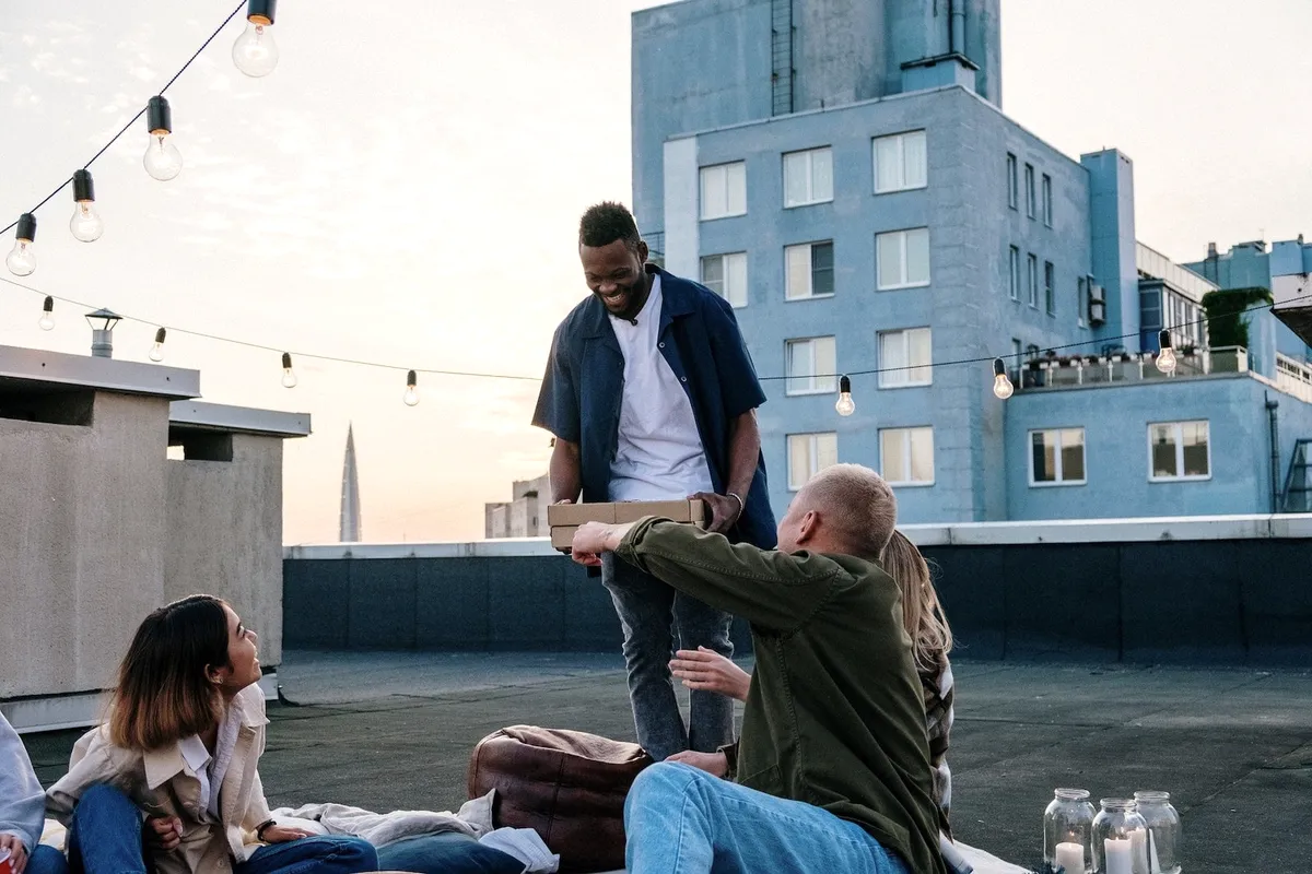 Friends sharing a pizza on a rooftop at sunset, string lights overhead.