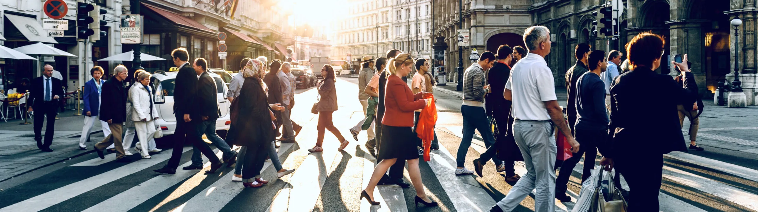 A crowd crossing a city street in the evening sun.