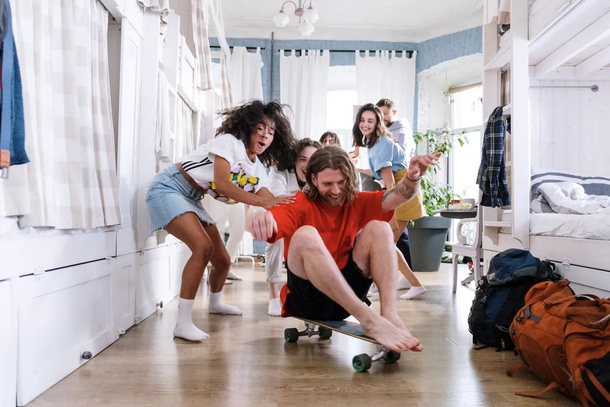 Friends playing with a skateboard in a dorm.