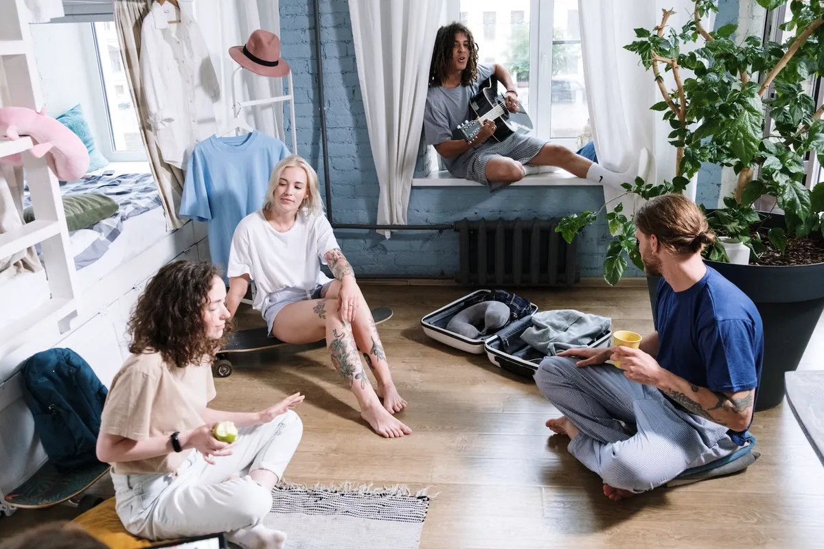 Friends sitting on the floor of a sunny room around a suitcase.