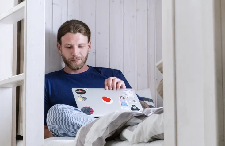 A man working on a laptop in a bunk bed.