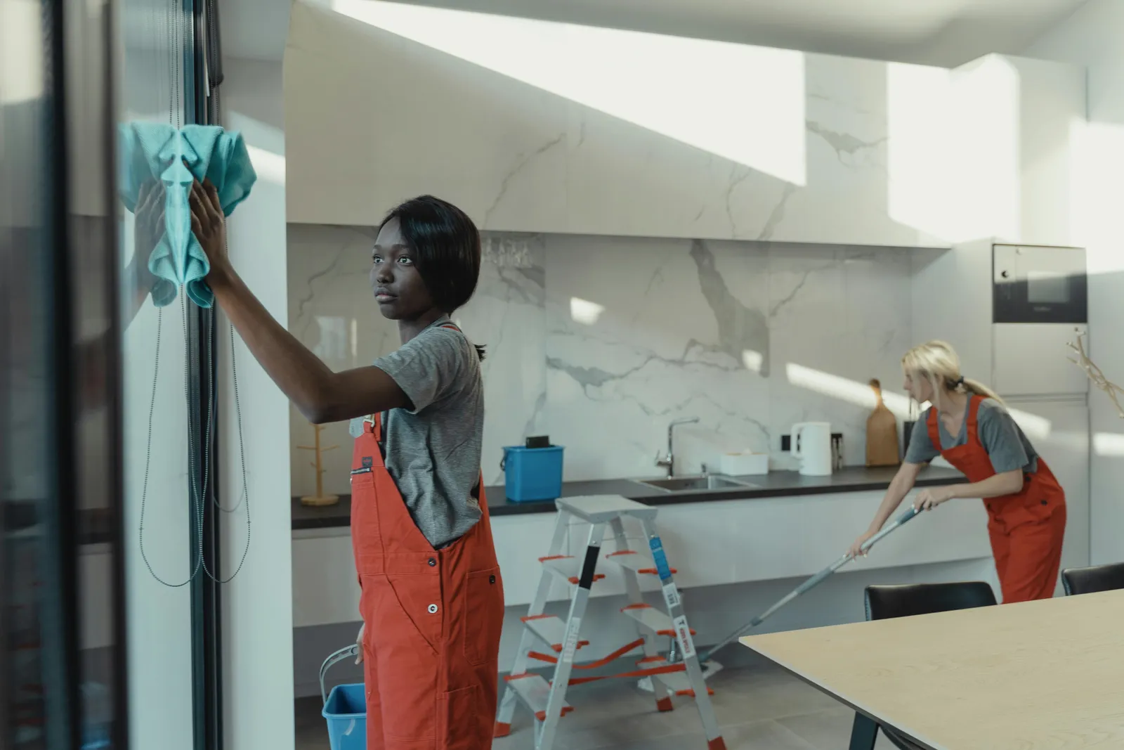 Two cleaners in red overalls at work in a white kitchen.