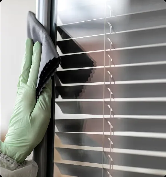 A gloved hand wiping a window blind.