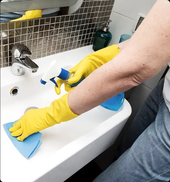 Yellow rubber gloves cleaning a bathroom sink.