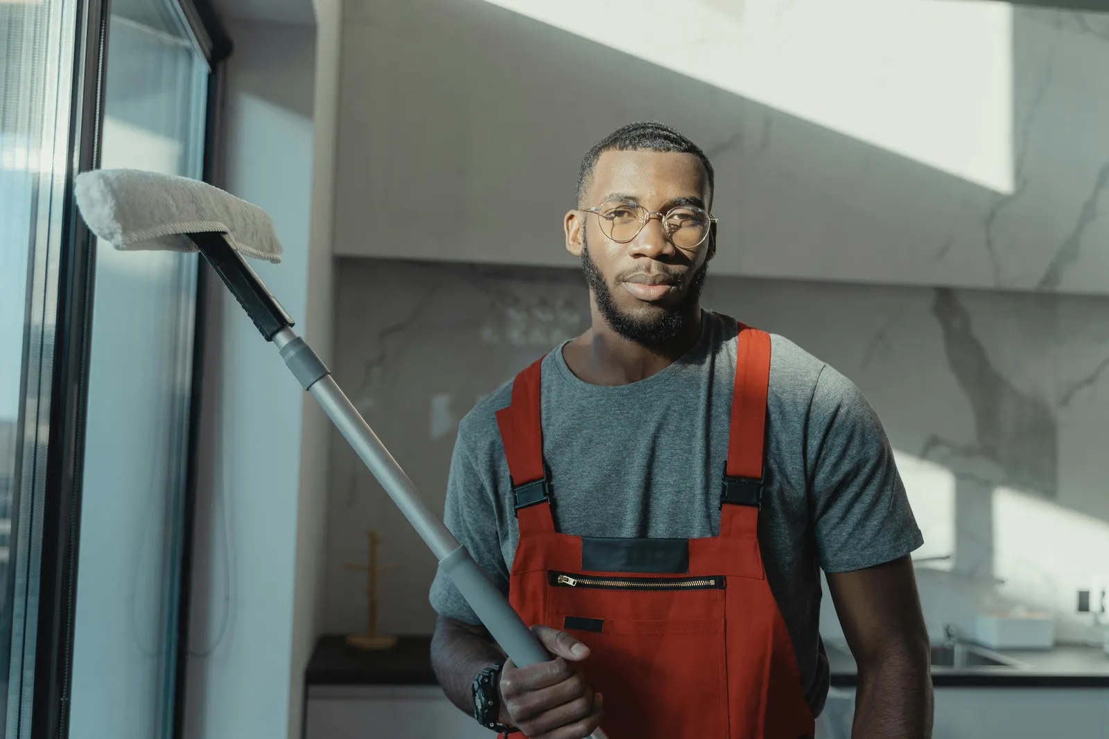 A cleaner in red overalls with a vacuum in a bright living room.
