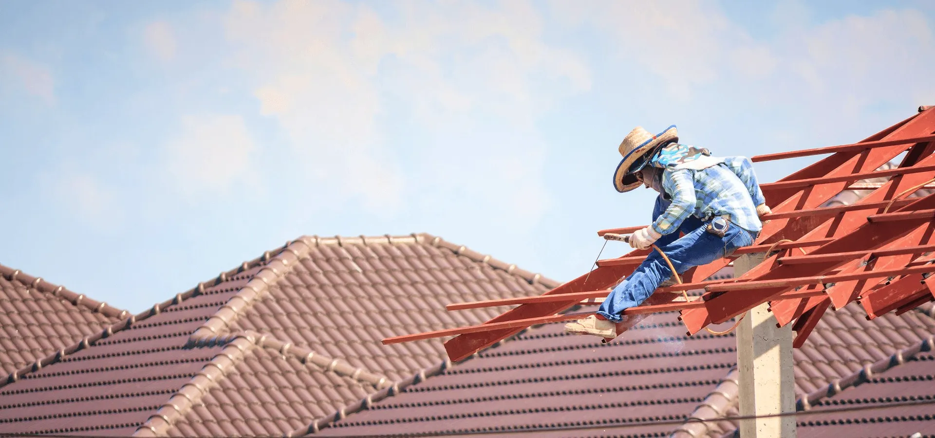 A roofer on red rafters under a soft sky.