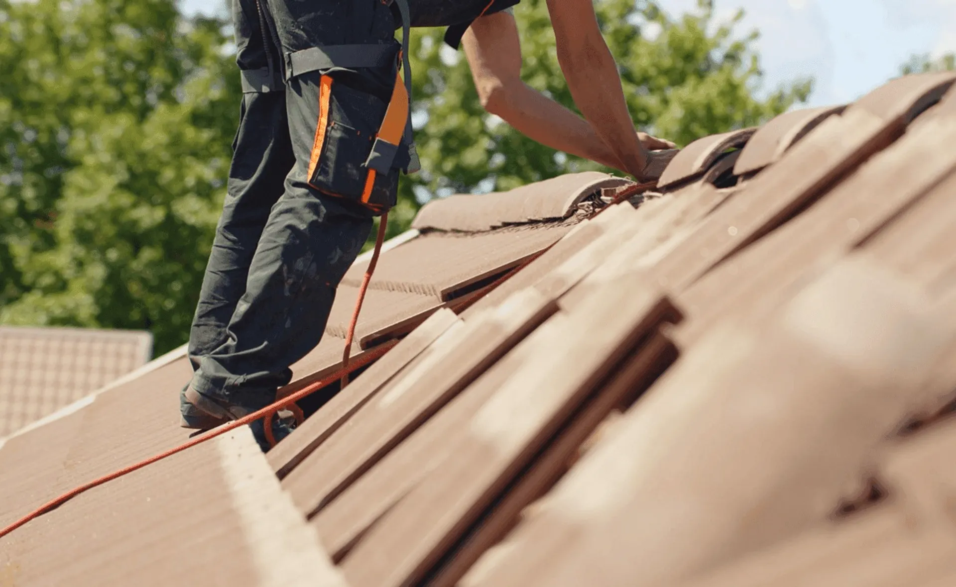 A roofer fitting tiles on a ridge, seen from below.