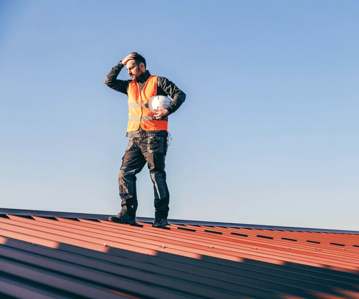 A roofer on a red roof against the sky.