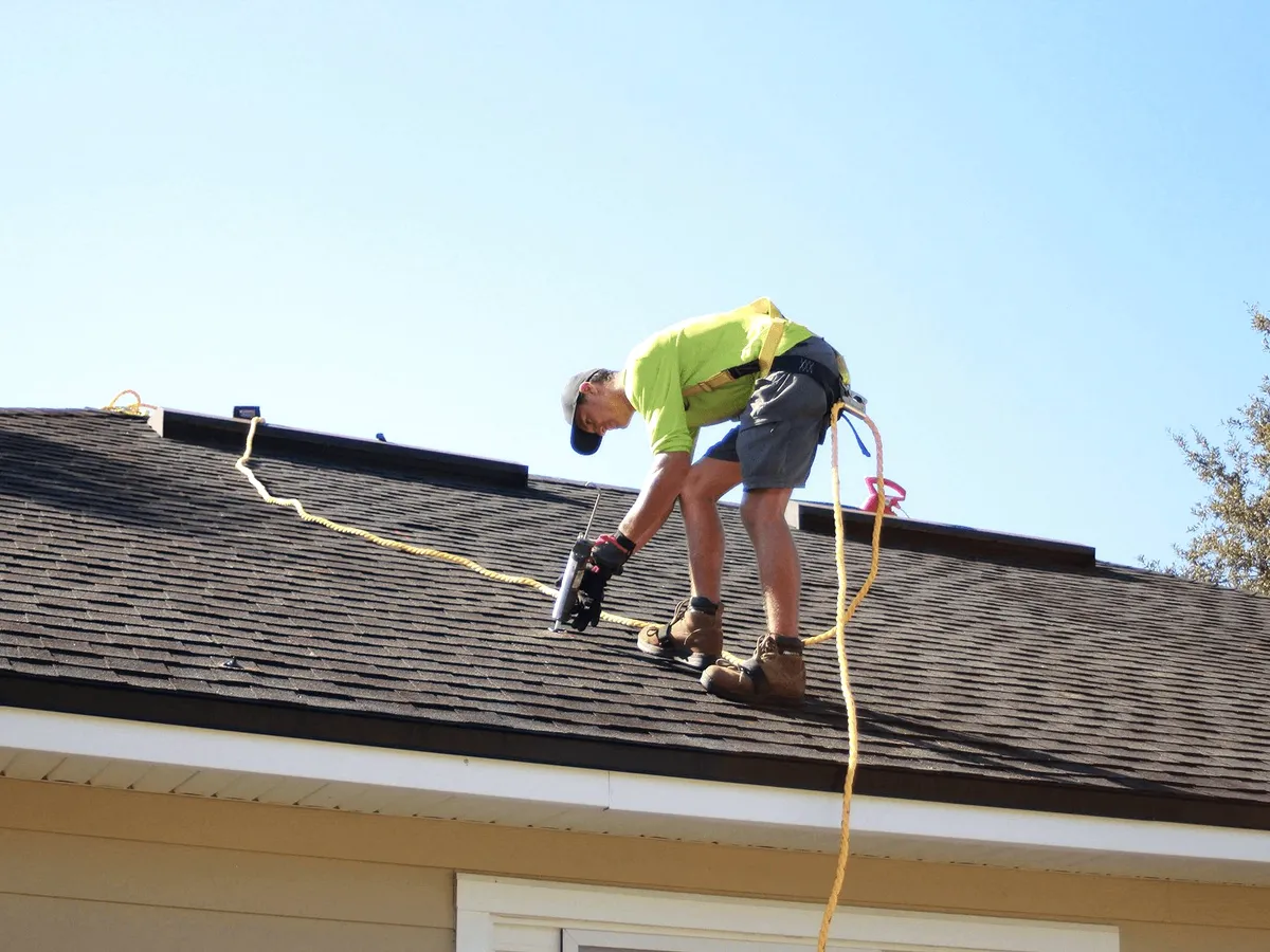 A roofer with a nail gun on shingles.