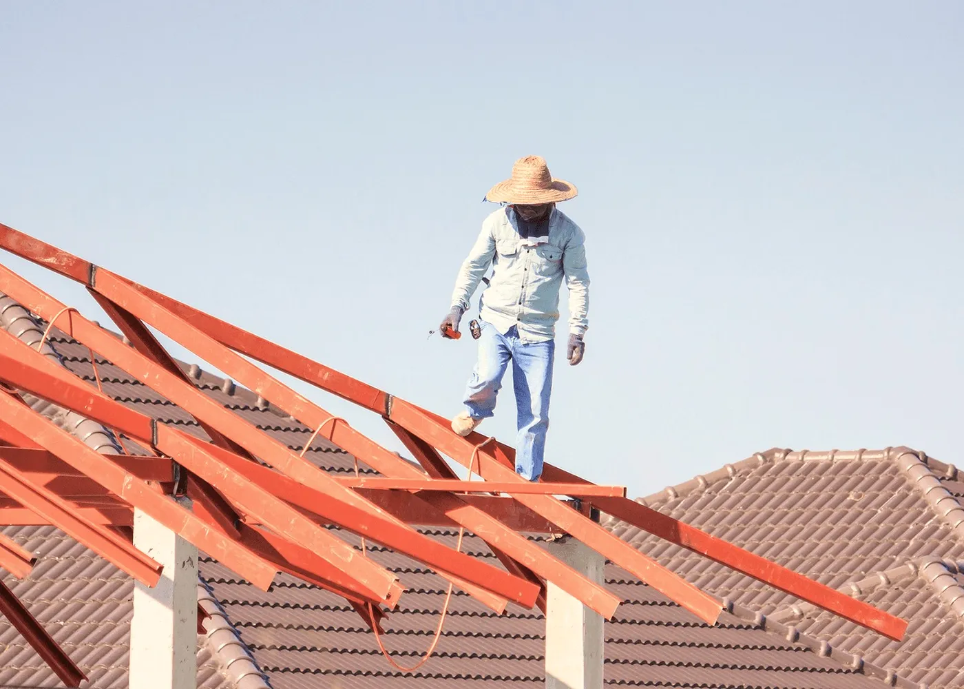 A roofer in a straw hat on red rafters.