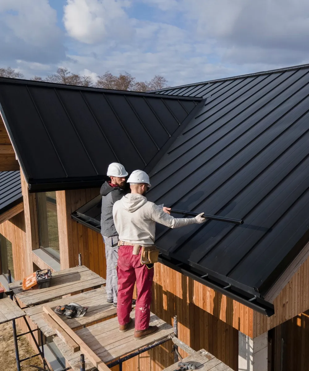 Two roofers on a dark metal roof.