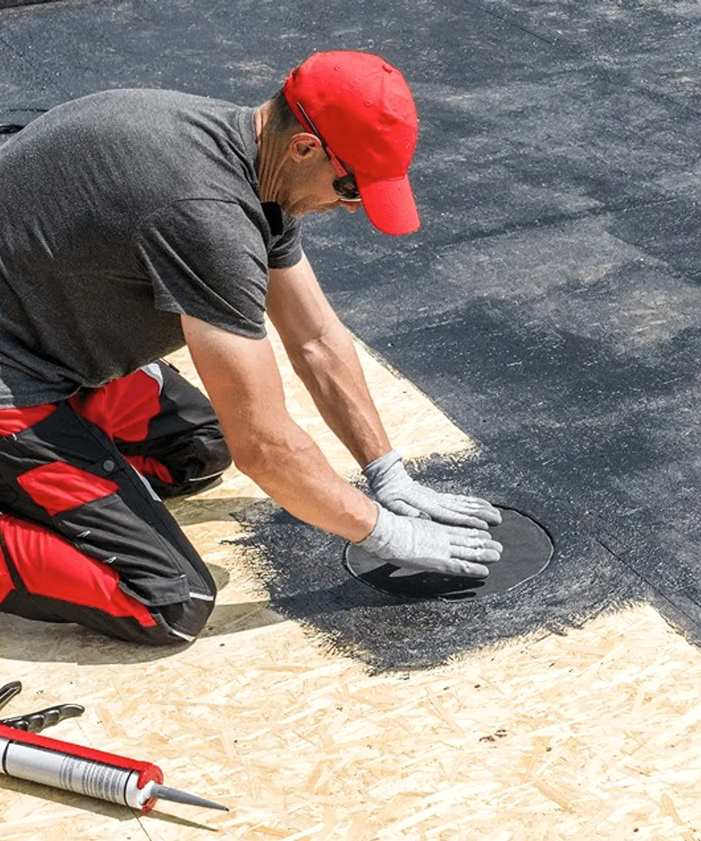 A roofer in a red cap on a flat roof.