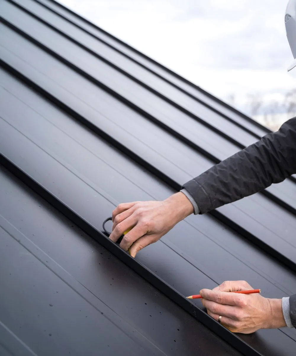 A roofer in a white helmet checking a seam.